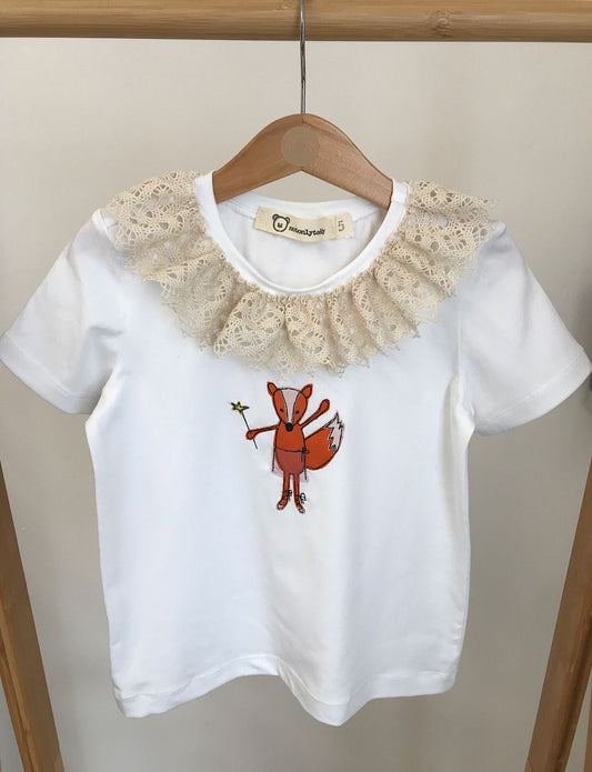 Maglietta a maniche corte bianca per bambina con ricamo di volpina ballerina e colletto arricciato in pizzo appesa